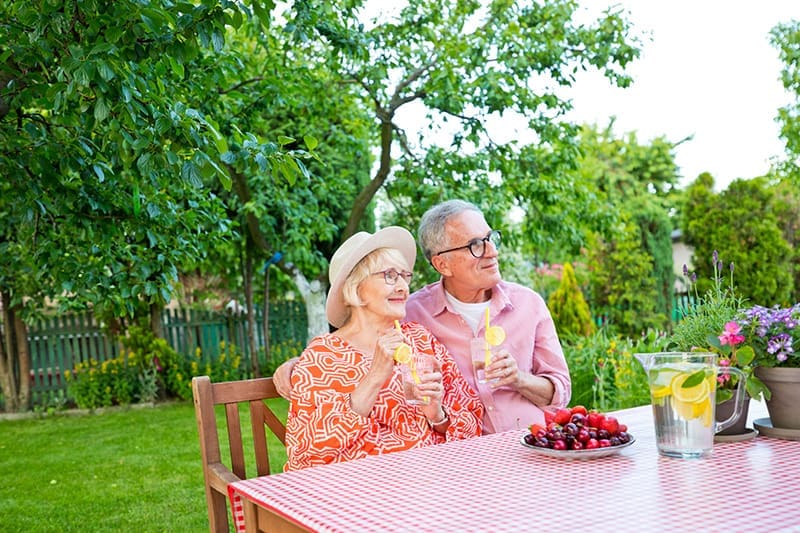 Thoughtful senior couple holding drinks while sitting at dining table in garden.